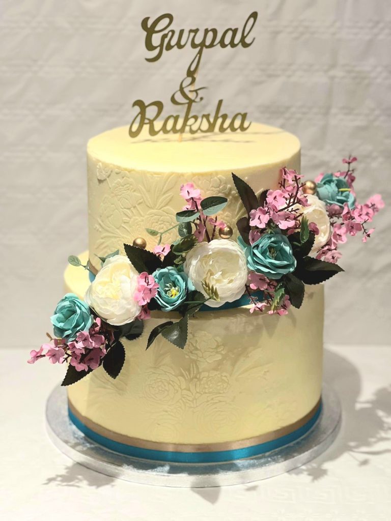 2 tier buttercream cake with artificial flowers and bespoke cake topper.
